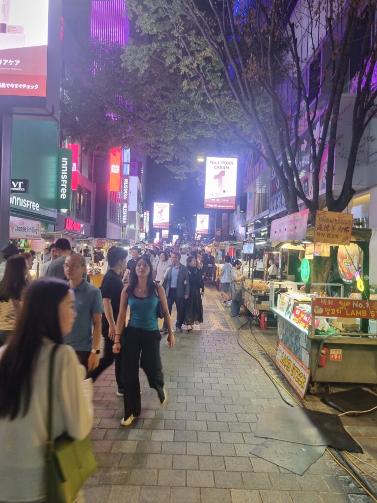 Busy Myeongdong street at night with food stalls, colorful signs, and crowds in Seoul