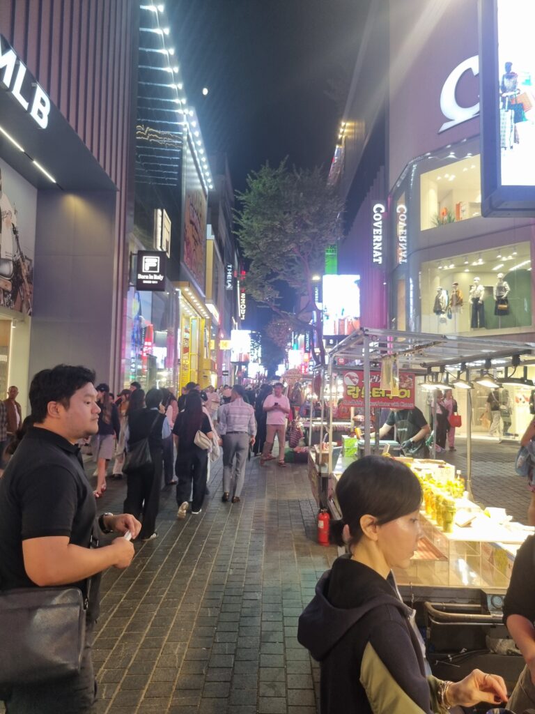 Busy Myeongdong shopping street at night with shops, food stalls, and pedestrians