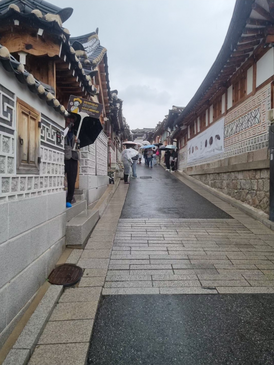 Scenic alleyway view of Bukchon Hanok Village lined with traditional hanok walls and tiled roofs on a rainy day